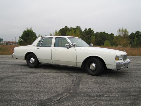 1991 Ford LTD Crown Victoria - This white sedan, likely a police vehicle, is captured from a front three-quarter perspective, its classic body style.