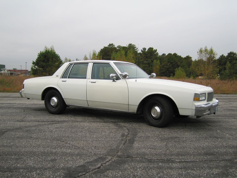 White sedan with chrome mirrors and police-style spotlights, viewed from the front three-quarter angle