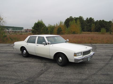 1991 Ford LTD Crown Victoria - This white sedan has a distinctive grille and body style typical of late 1980s Chevrolet models.