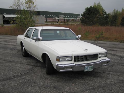 1991 Ford LTD Crown Victoria - This white sedan features a prominent chrome grille and a visible license plate.
