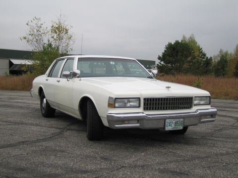 1991 Ford LTD Crown Victoria - This white sedan features a prominent chrome grille and dual rectangular headlights, typical of 1980s American sedans.