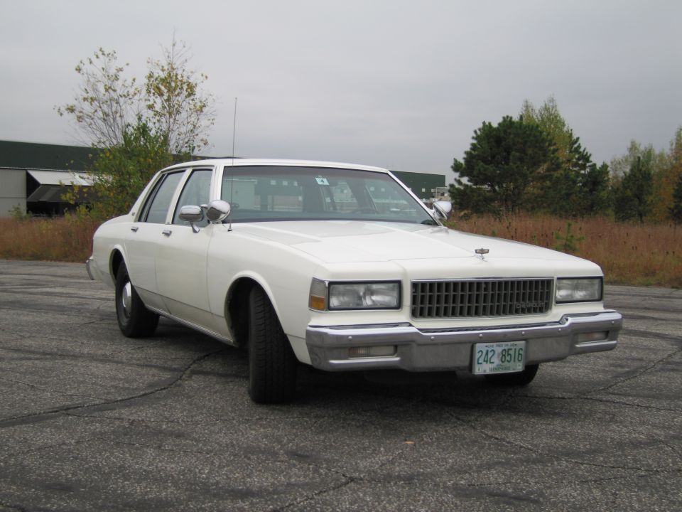 White 1980s sedan with chrome grille and rectangular headlights parked outdoors