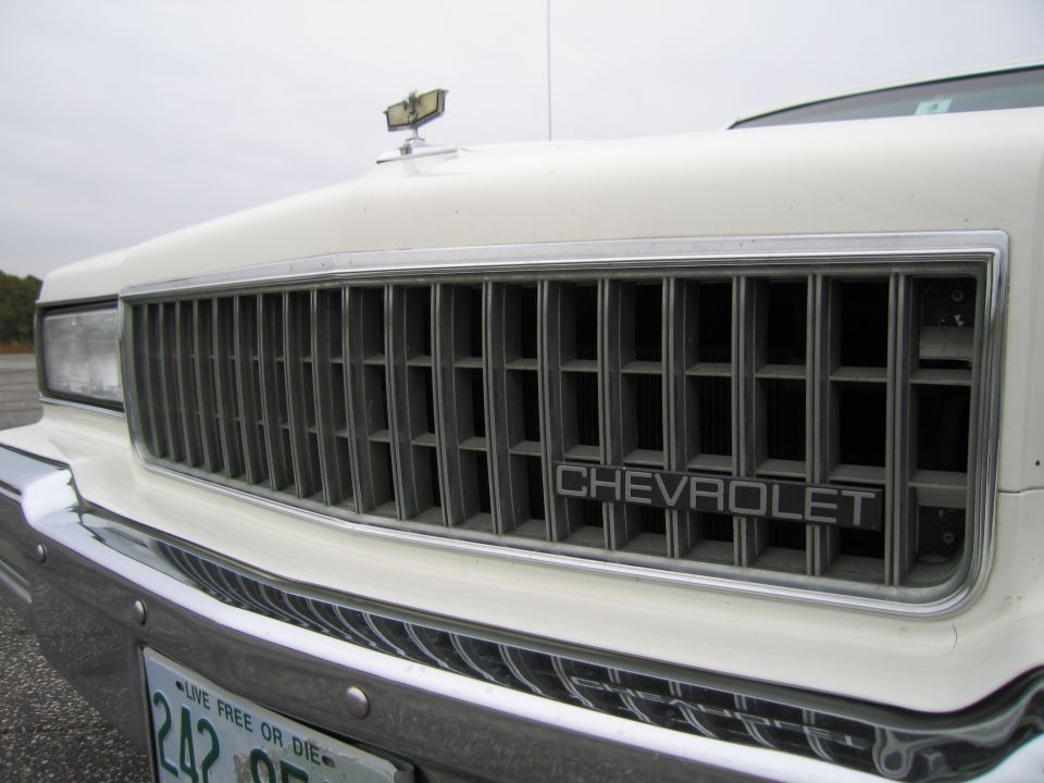 Close-up of a white Chevrolet's front grille with the Chevrolet nameplate visible. A hood ornament is on top