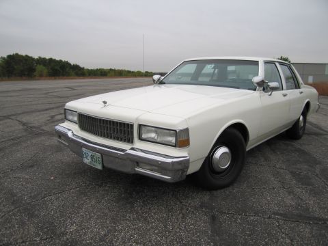 1991 Ford LTD Crown Victoria - This white sedan features a prominent chrome grille and dual square headlights, typical of 1980s American sedans.