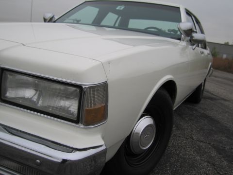 1991 Ford LTD Crown Victoria - Close-up of a white sedan's front passenger side, revealing its classic grille and headlight design.