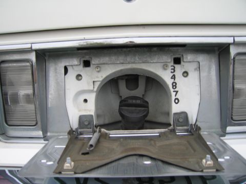 1991 Ford LTD Crown Victoria - The fuel filler door of a white 1991 Ford Crown Victoria LTD is open, revealing the gas cap and a series of stamped numbers.