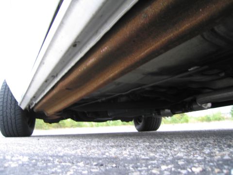 1991 Ford LTD Crown Victoria - The undercarriage of a white vehicle reveals significant rust on the rocker panel and exhaust system.