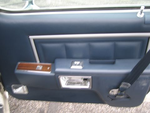 1991 Ford LTD Crown Victoria - The interior door panel features quilted blue upholstery, a wood grain trim piece, and chrome hardware for the window crank and door handle.