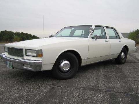 1991 Ford LTD Crown Victoria - This white 1990 Chevrolet Caprice sedan, equipped with police spotlights and an antenna, is shown from a 3q front angle.