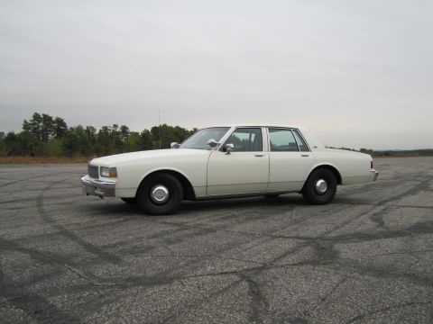 1991 Ford LTD Crown Victoria - This white sedan, likely from the 1980s, is seen from the side on an empty lot.