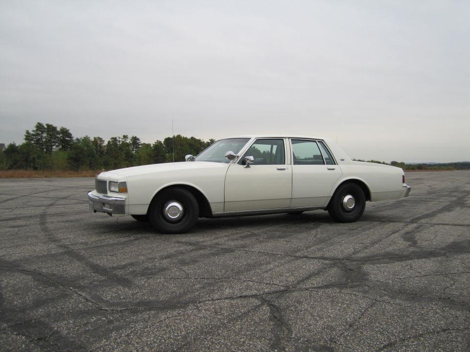 White sedan parked on cracked asphalt with tire marks, side view