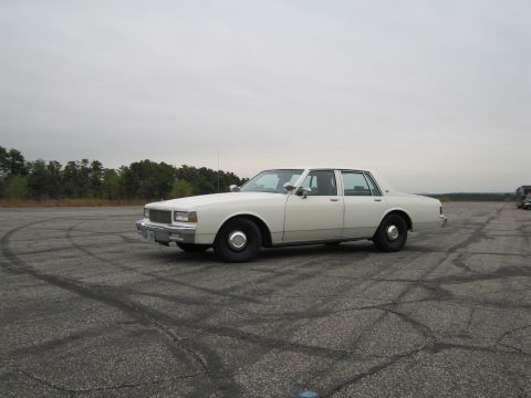 1991 Ford LTD Crown Victoria - This white 1990 Chevrolet Caprice sedan is seen from a three-quarter front view on a cracked asphalt lot.