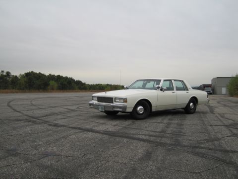 1991 Ford LTD Crown Victoria - A white sedan sits on a cracked asphalt lot under an overcast sky.