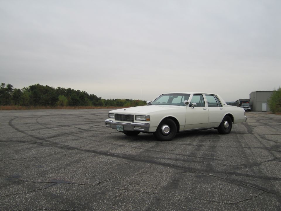 White sedan parked on asphalt with tire marks. Building and trees in background