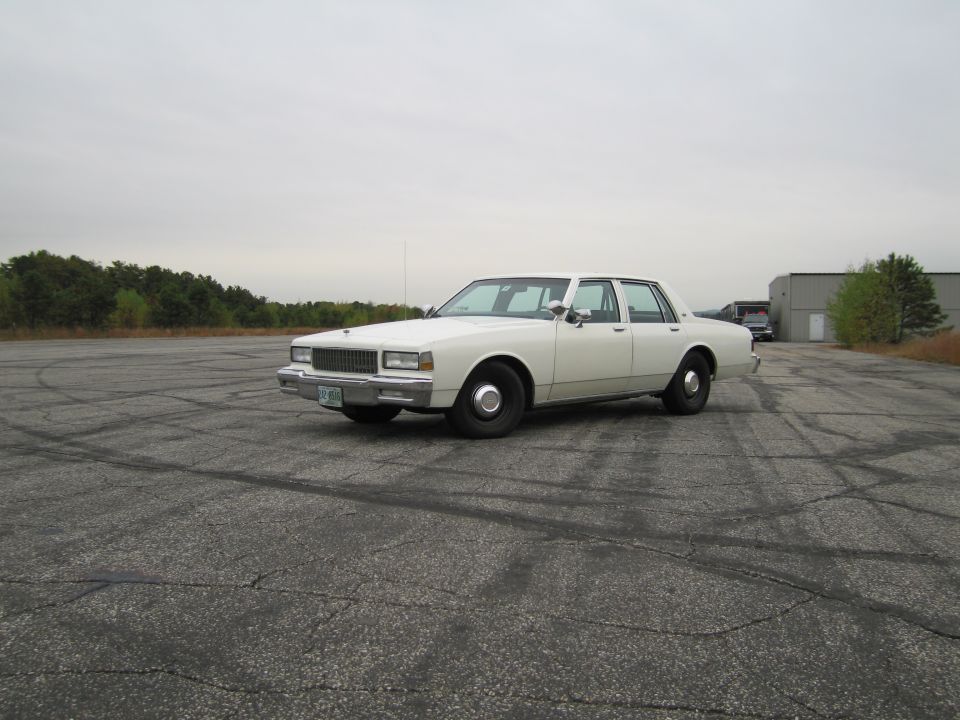 White sedan parked on cracked asphalt, front three-quarter view
