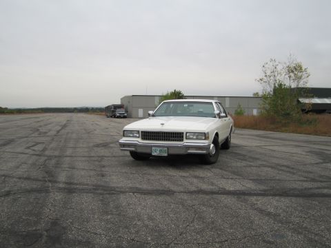 1991 Ford LTD Crown Victoria - This white 1990 Chevrolet Caprice sedan is seen from the front on an overcast day in an industrial area.