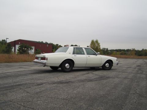 1991 Ford LTD Crown Victoria - Side view of a white sedan parked outdoors on a cloudy day.