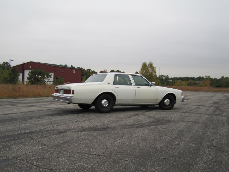 White sedan parked on cracked asphalt lot with a red building in the background
