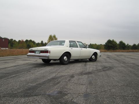 1991 Ford LTD Crown Victoria - This white sedan, likely a 1990 Chevrolet Caprice, is viewed from its rear-left quarter in an empty lot.