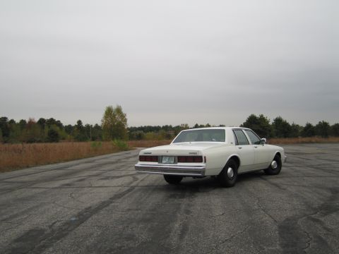 1991 Ford LTD Crown Victoria - White sedan parked on cracked asphalt under an overcast sky.