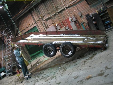 1900 Ford C-350 (Centurion Conversions) - Workshop scene with a trailer suspended by a hoist, showing some snow on its deck.