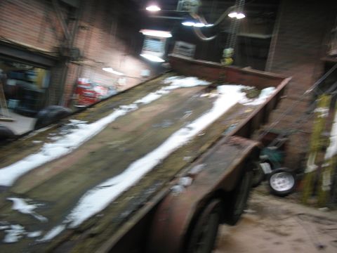 1900 Ford C-350 (Centurion Conversions) - A trailer sits in a dimly lit workshop, its deck partially covered in snow and dirt.