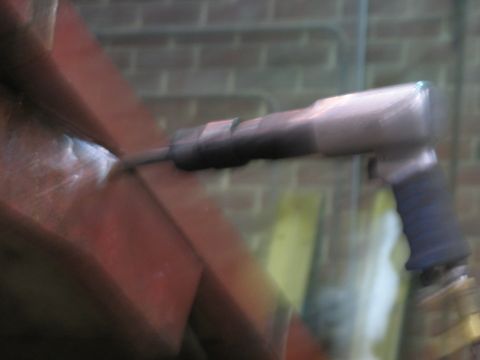 1900 Ford C-350 (Centurion Conversions) - A pneumatic hammer is used on red metal beams, with a brick wall visible behind.