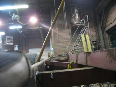 1900 Ford C-350 (Centurion Conversions) - The underside of a vehicle frame is shown in a workshop setting, with a tire in the foreground.