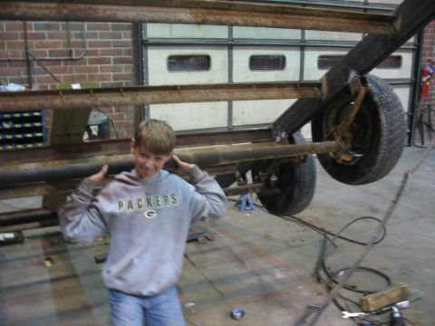 1900 Ford C-350 (Centurion Conversions) - A young boy stands in front of a trailer chassis in a workshop.