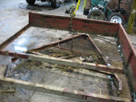 1900 Ford C-350 (Centurion Conversions) - Trailer frame in disrepair, showing rust and debris. A chain hoist is suspended above.