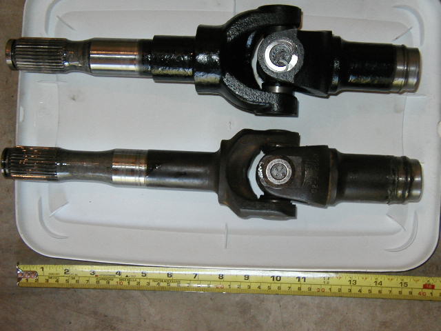 Two splined axle stub shafts with U-joints on white tray, tape measure below