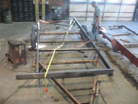 1900 Ford C-350 (Centurion Conversions) - A trailer frame is under construction in a workshop, with welding equipment nearby.