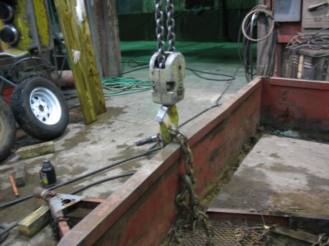 1900 Ford C-350 (Centurion Conversions) - A hoist chain is attached to the edge of a red trailer bed in a workshop setting.
