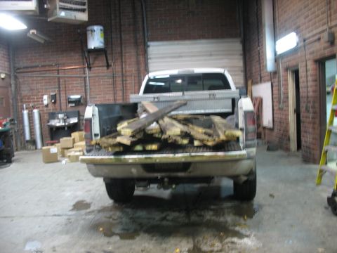 1900 Ford C-350 (Centurion Conversions) - A white pickup truck is parked inside a garage, its bed filled with lumber and a metal toolbox.