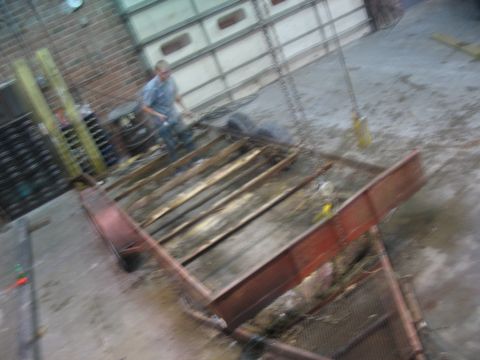 1900 Ford C-350 (Centurion Conversions) - A red trailer frame with wooden slats is seen in a garage setting, with a person in the background.
