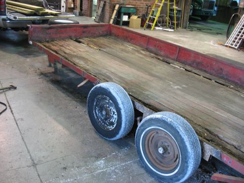 1900 Ford C-350 (Centurion Conversions) - A red flatbed trailer with a worn wooden deck and dual wheels sits in a workshop.