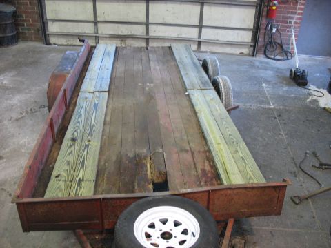 1900 Ford C-350 (Centurion Conversions) - A utility trailer sits in a garage, its wooden deck showing signs of wear and recent repairs with new lumber.