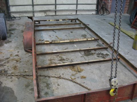 1900 Ford C-350 (Centurion Conversions) - A rusty trailer frame with wooden slats is suspended by chains in a workshop.