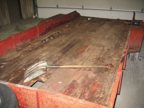 1900 Ford C-350 (Centurion Conversions) - A red trailer with a worn wooden deck and a shovel lying on it sits in a garage.