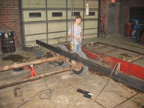 1900 Ford C-350 (Centurion Conversions) - Trailer frame assembly in progress, with a young person operating a hoist in a workshop.