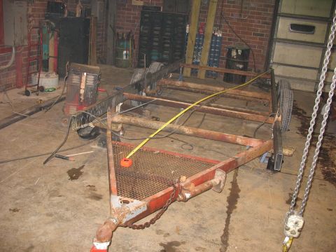 1900 Ford C-350 (Centurion Conversions) - Workshop scene showing a rusty trailer frame with a measuring tape, surrounded by tools and equipment.