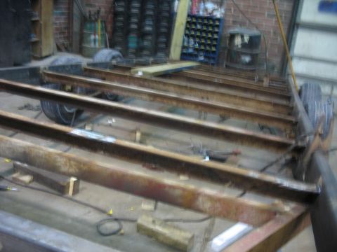 1900 Ford C-350 (Centurion Conversions) - A partially constructed trailer frame is visible, supported by wooden blocks in a workshop setting.
