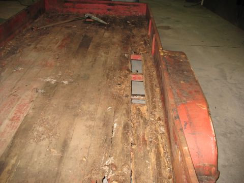 1900 Ford C-350 (Centurion Conversions) - The wooden deck of a trailer shows significant wear and damage, with exposed metal supports and debris scattered across the surface.
