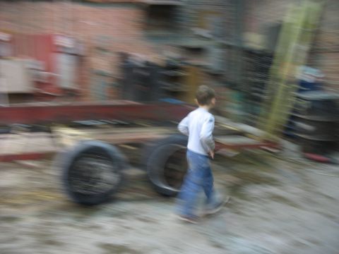 1900 Ford C-350 (Centurion Conversions) - A child walks past a trailer chassis in a cluttered outdoor area.