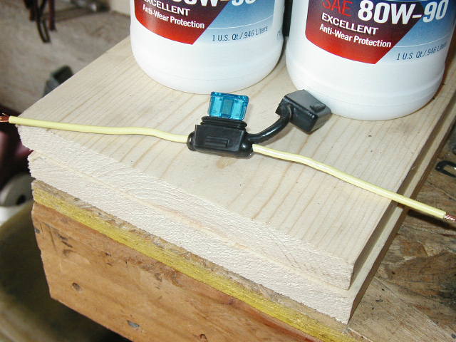 Inline blade fuse holder with blue fuse on yellow wire, gear oil bottles behind