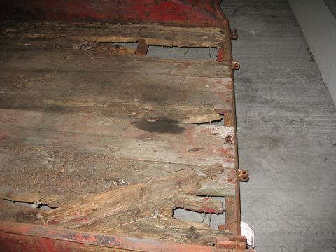 1900 Ford C-350 (Centurion Conversions) - The wooden deck of a trailer shows significant rot and damage, with holes exposing the underlying structure.