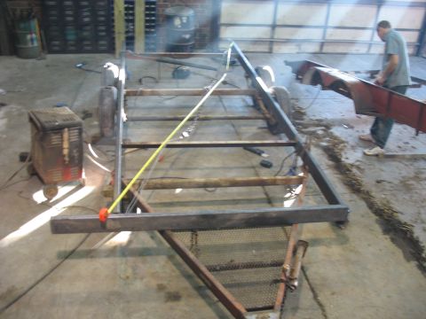 1900 Ford C-350 (Centurion Conversions) - A trailer frame is being constructed in a workshop, with welding equipment and a person assembling parts.