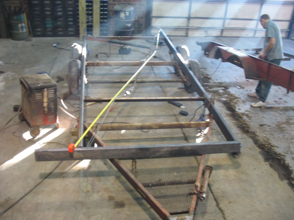 Trailer frame construction with welding equipment and a person working on a red fender
