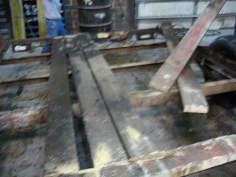 1900 Ford C-350 (Centurion Conversions) - The image shows the interior of a workshop or garage, focusing on a trailer bed with scattered wooden planks and debris.