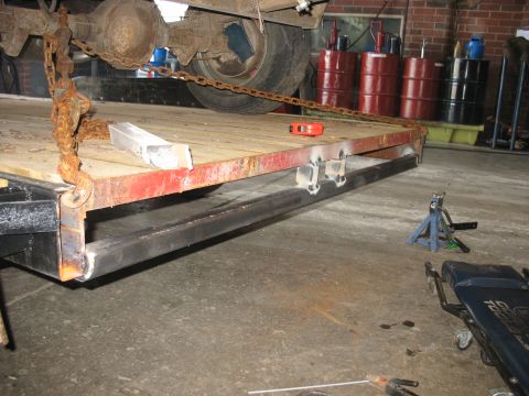 1900 Ford C-350 (Centurion Conversions) - A trailer is shown with a vehicle axle suspended by rusty chains, with red side panels and metal bracing.